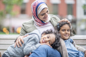 A muslim mother smiles with her children in her lap while sitting on a bench. They are all intertwined and happy to be spending time together. |