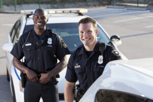Multi-ethnic police officers (20s) standing in front of police car.
