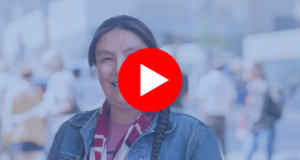 A First Nations woman is smiling in front of a crowd of people.