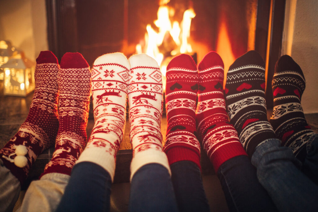 Feet in Christmas socks near fireplace.  Four pair of feet warming up. Friends at cozy winter vacation. |