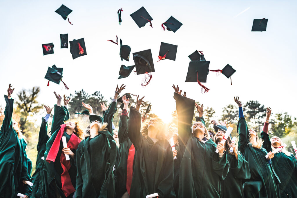 Un grand groupe d'étudiants heureux célébrant leur jour de remise de diplôme en plein air tout en jetant leurs casquettes en l'air.