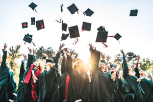 Un grand groupe d'étudiants heureux célébrant leur jour de remise de diplôme en plein air tout en jetant leurs casquettes en l'air.