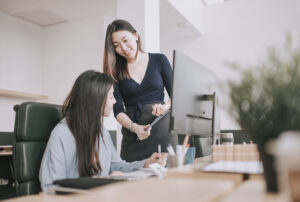 2 asian chinese white collar women having discussion in open plan office looking at files stock photo