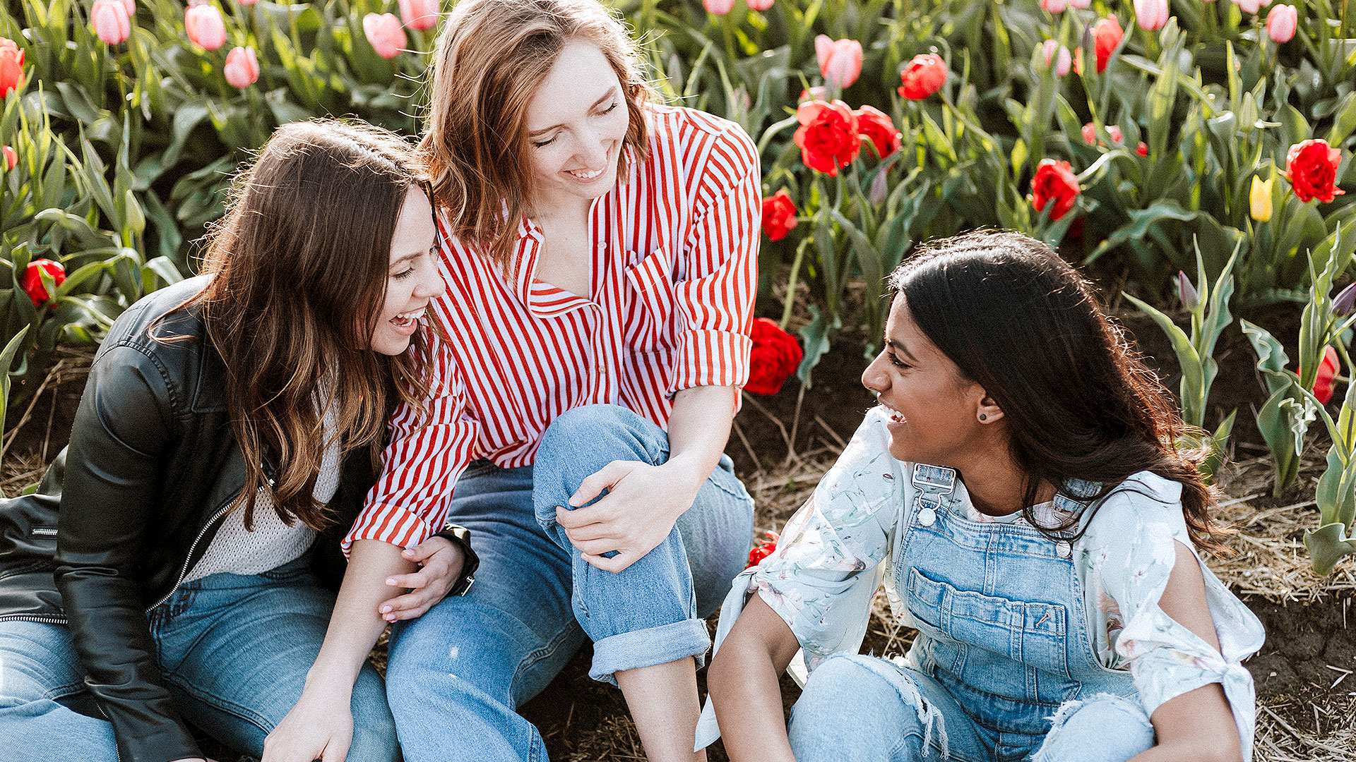 three young women sitting in a field of tulips having fun