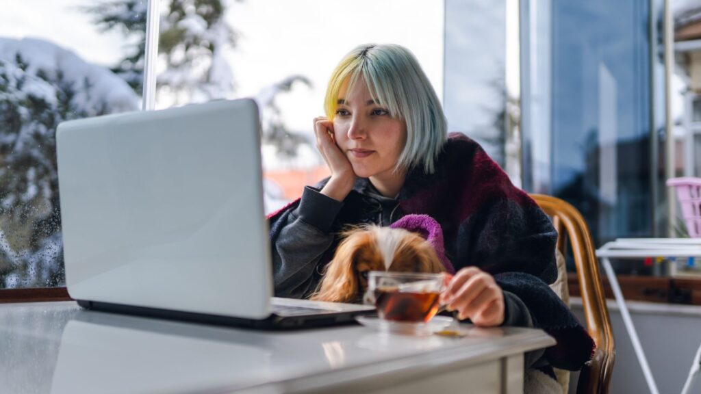 a young woman sits in front of the laptop with a cup of tea besides her