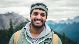 You man hiking with a backpack and posting with range of mountain in the background