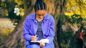 A young woman writes in the journal while sitting in the park