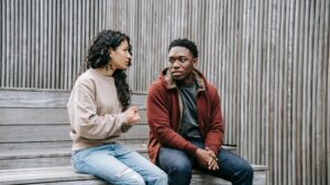 Une jeune femme parle à un homme assis sur un escalier en bois