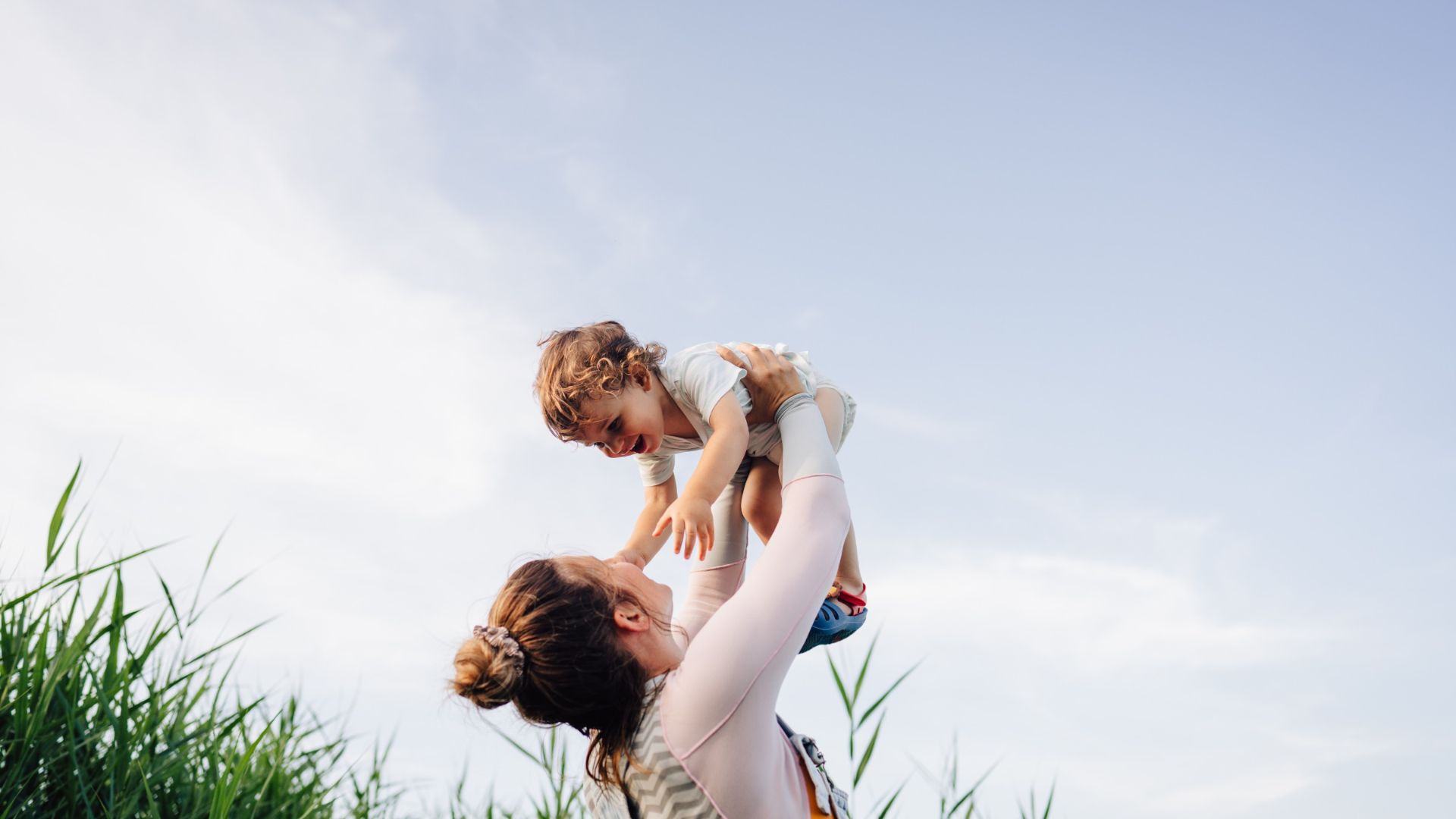 A woman holds her child up with a blue sky in the background