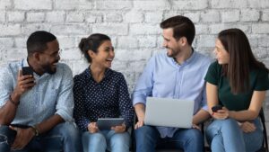 Quatre jeunes assis sur un banc contre un mur de briques blanches parlant et riant