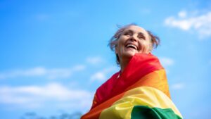 An older woman wrapped into a rainbow-colored flag smiles