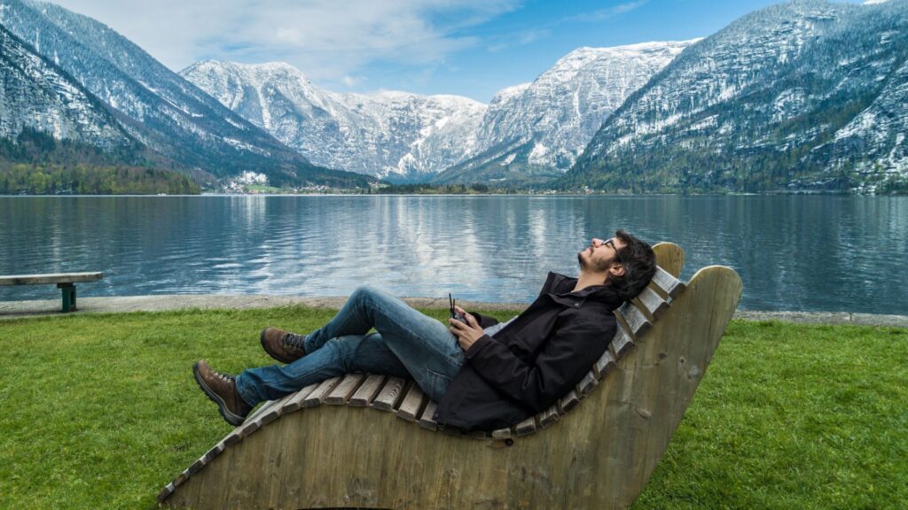 Un homme est assis sur une chaise en bois devant un lac.