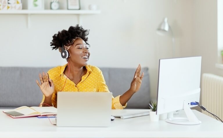 Happy African American Businesswoman Having Fun While Working at Office Desk and Listening Music Over Headphones.