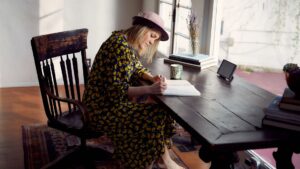 A female individual in a business setting, calmly engaged in the act of writing in a book at her desk.
