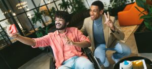 Mixed race Executive Associates Meeting in Office Reception Room making funny selfies with smartphone. Disabled indian businessman in wheelchair and latin american partner