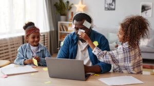 A father is playing with two daughters sitting in front of the computer