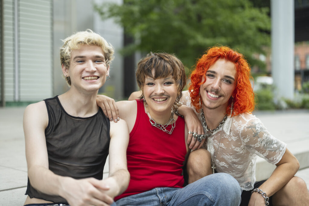 Trois amis aux coiffures colorées souriant et posant ensemble à l'extérieur.
