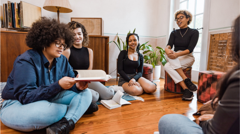 Plusieurs jeunes femmes assises par terre, les jambes croisées, absorbées par la lecture de livres ensemble.