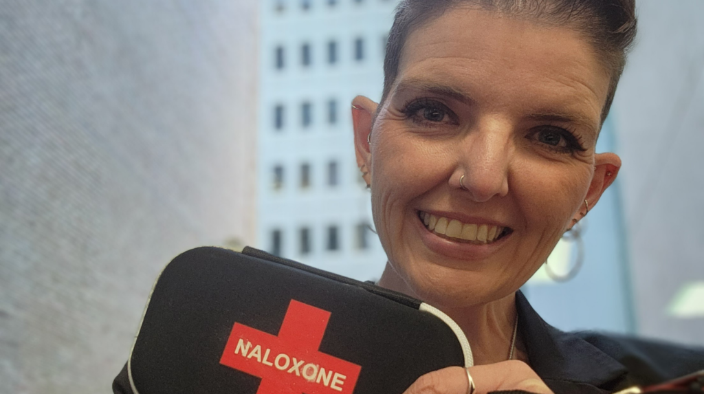 A smiling woman holding a Naloxone kit in her hand