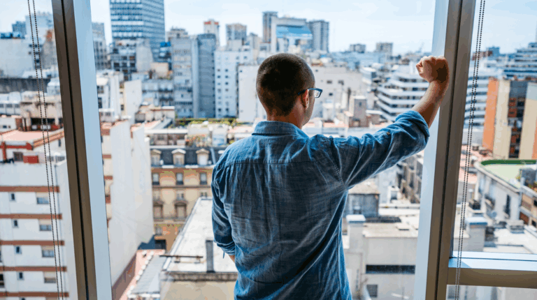 Un homme regarde par la fenêtre d'un appartement et fixe la ville.