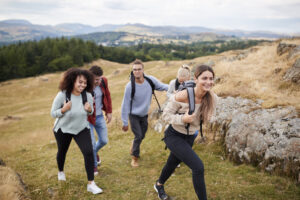 group of five young adult friends hiking across a field uphill towards the summit