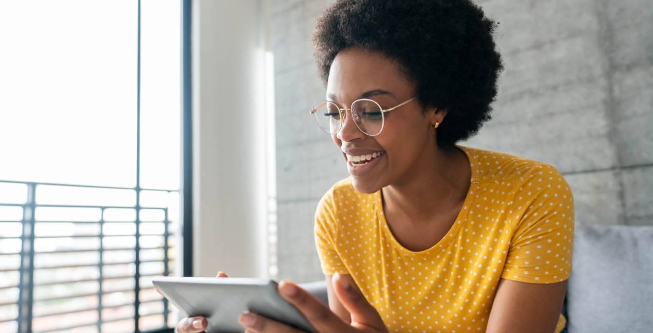 Main Image Une femme assise sur son canapé qui profite des médias sur sa tablette.