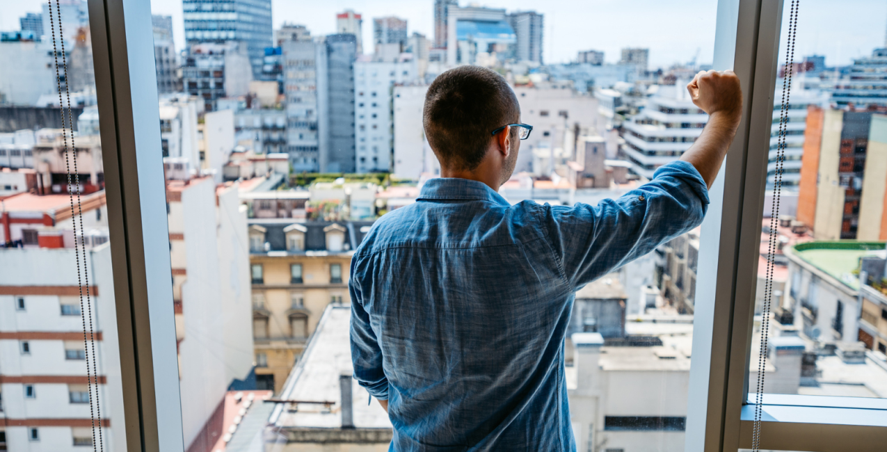 Un homme regarde par la fenêtre d'un appartement et fixe la ville.