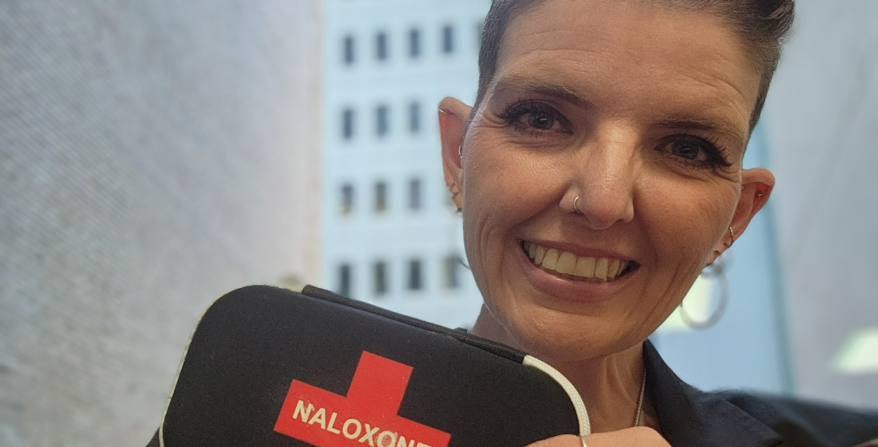 A smiling woman holding a Naloxone kit in her hand